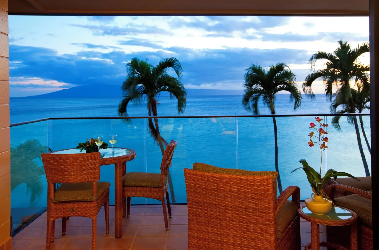 Oceanfront balcony with wicker seating, palms, and evening ocean view at Napili Kai Beach Resort.