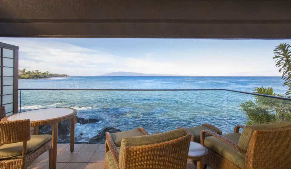 Oceanfront suite balcony with wicker chairs and wide water view at Napili Kai Beach Resort.