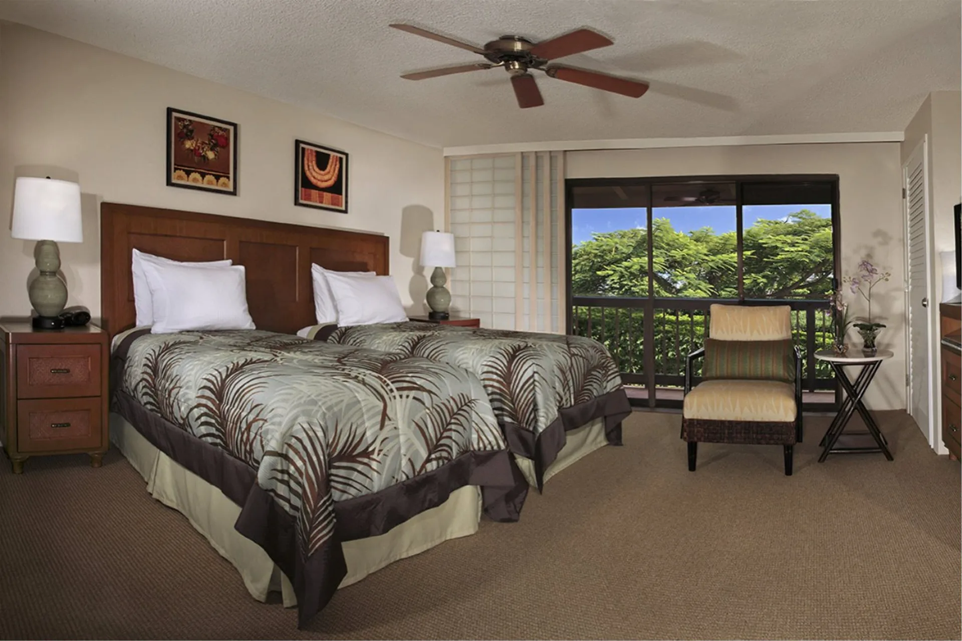 Two-bed guest room in an oceanfront suite at Napili Kai Beach Resort with balcony doors and greenery.