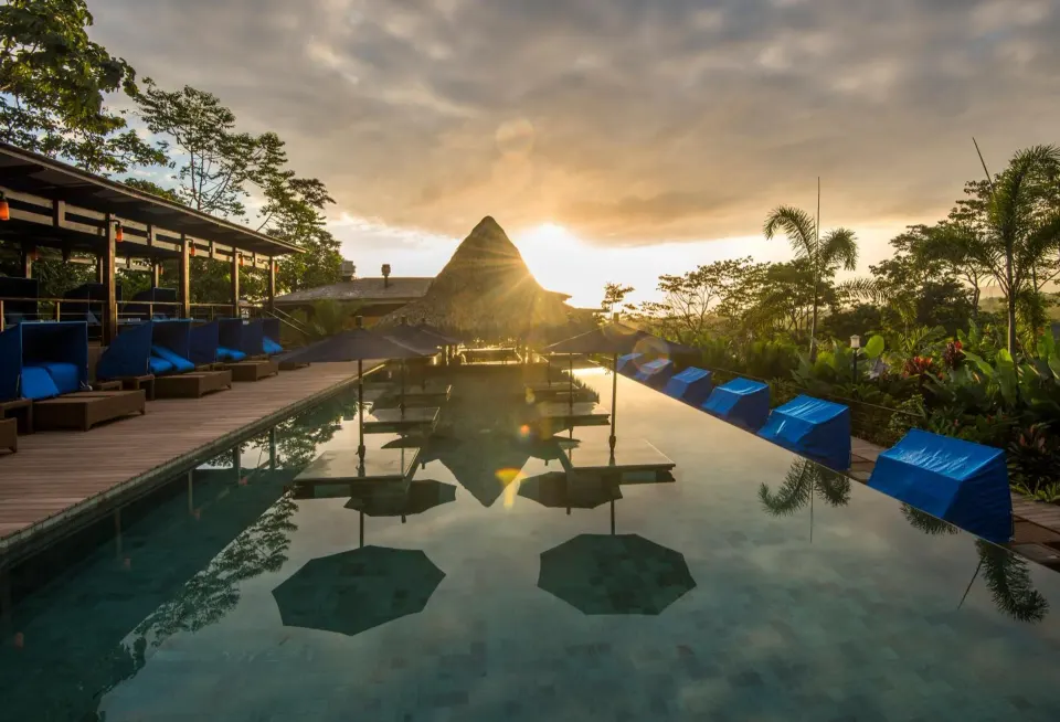 Resort pool at sunset with loungers and umbrellas at Nayara Springs.