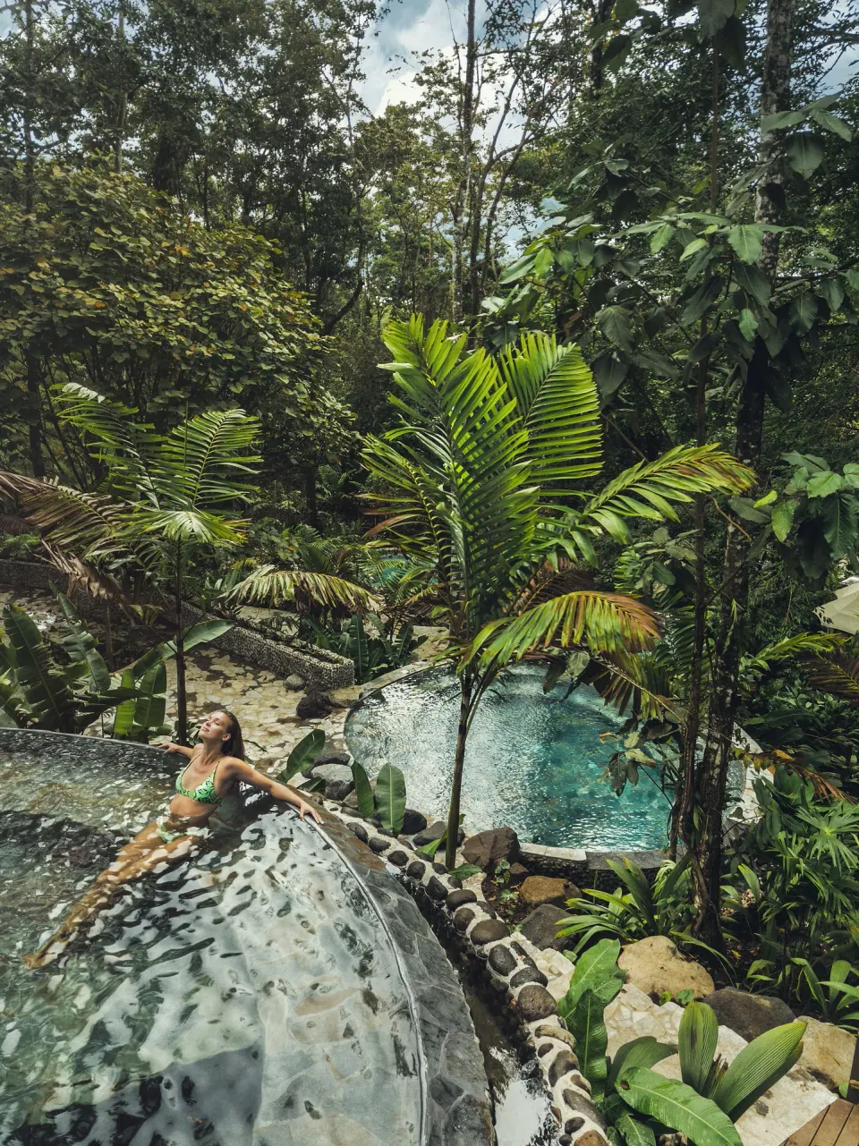 Guest in a jungle hot spring pool among tropical plants at Nayara Springs.