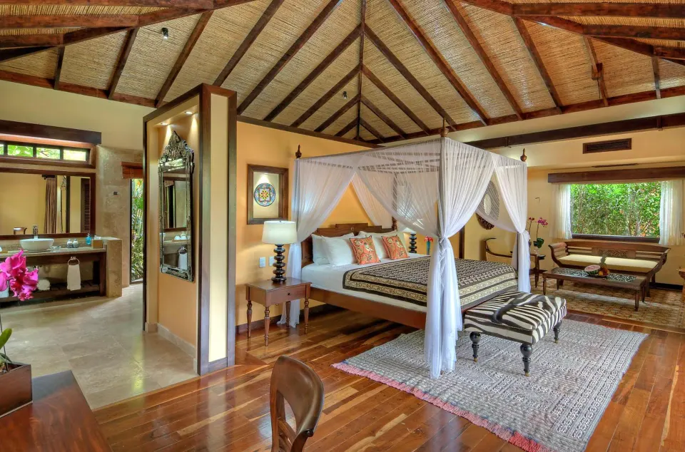 Spacious villa bedroom with a canopy king bed and open bathroom at Nayara Springs.