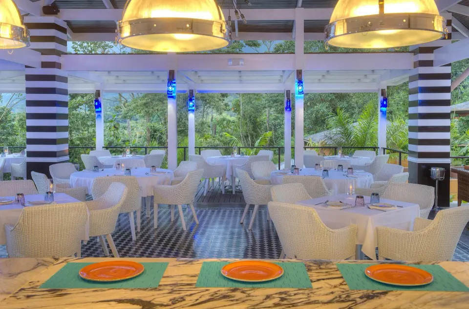 White dining chairs and round tables fill an airy restaurant at Nayara Springs.