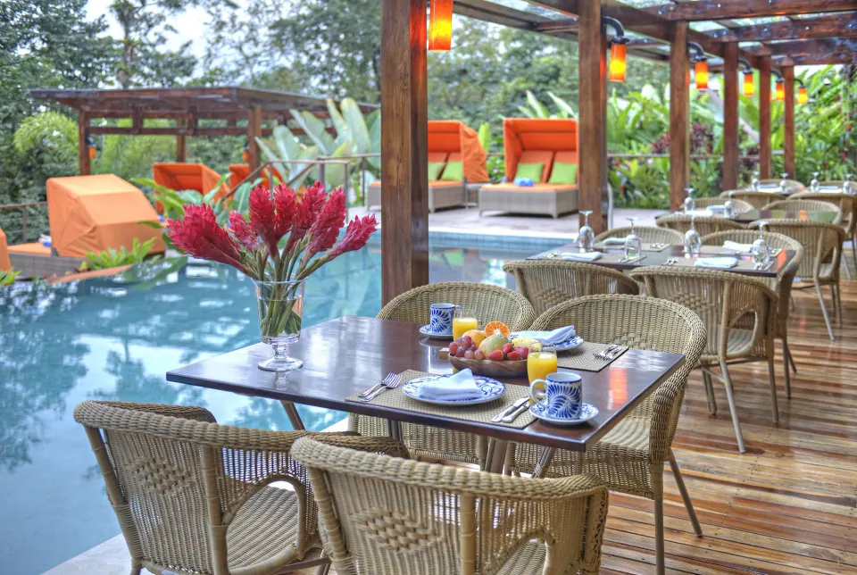 Poolside dining tables beside orange loungers at Nayara Springs.