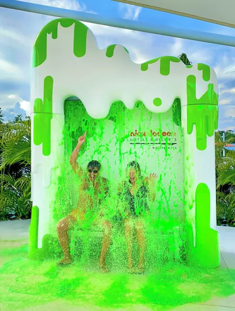 Two guests sit under a green slime shower at Nickelodeon Hotels & Resorts Riviera Maya.