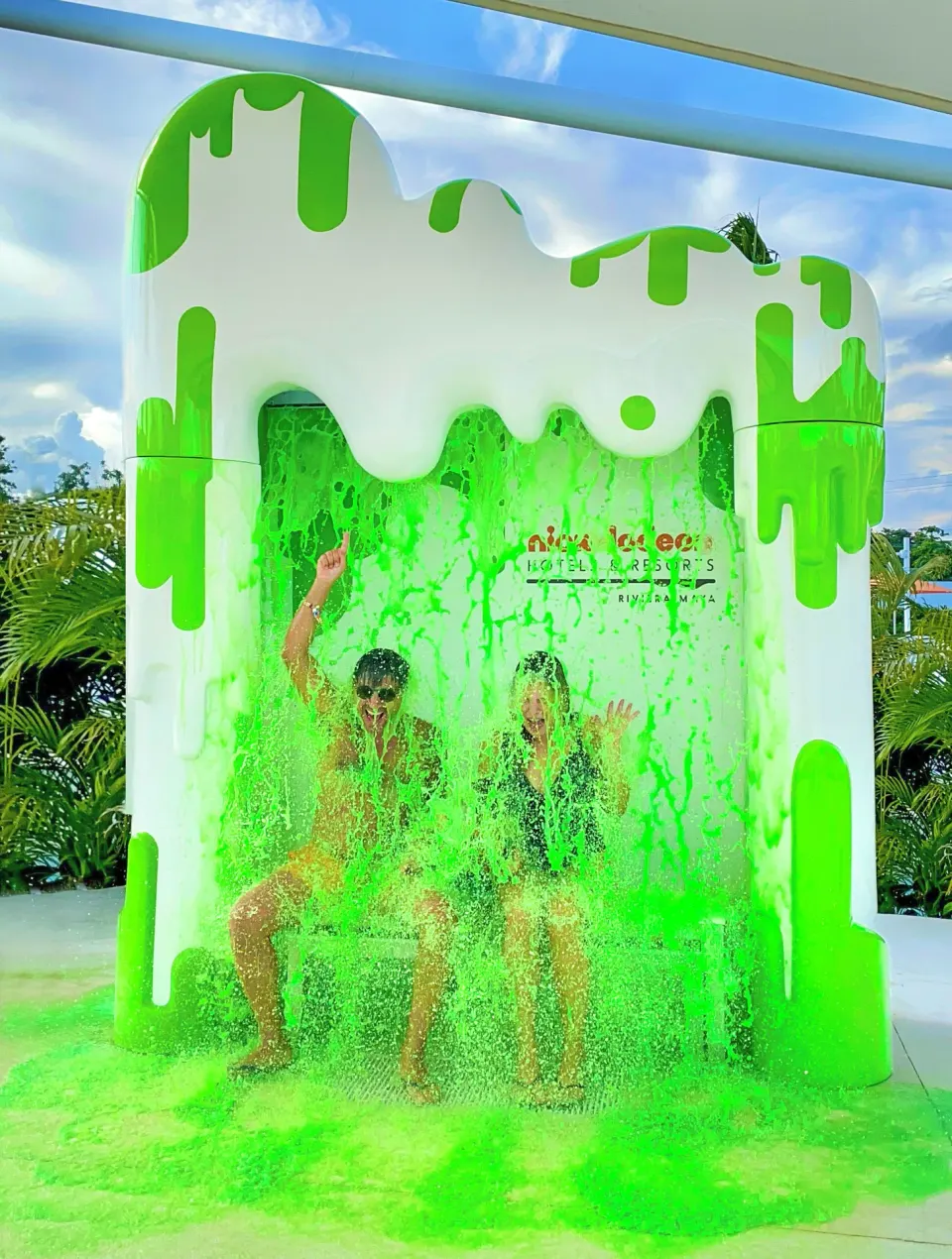 Two guests sit under a green slime shower at Nickelodeon Hotels & Resorts Riviera Maya.