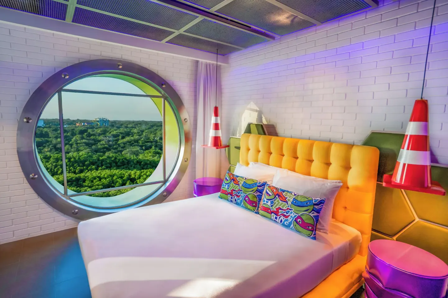 Lair Suite bedroom with round window, king bed, and colorful turtle pillows at Nickelodeon Hotels & Resorts Riviera Maya.
