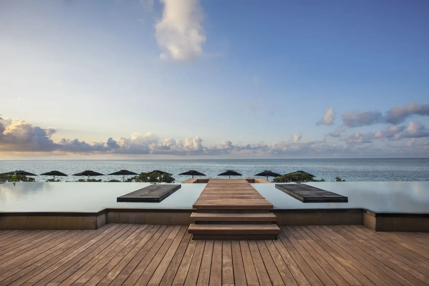 A wooden walkway crosses an infinity pool toward the ocean at Nizuc Resort and Spa.