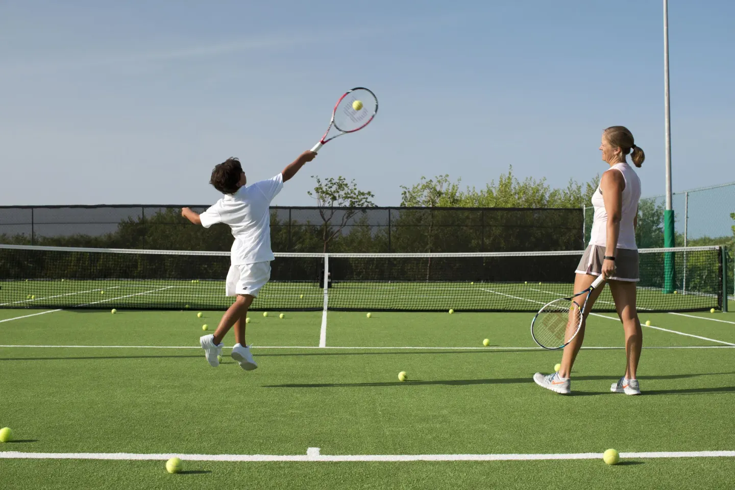 Adult and child playing tennis on an outdoor court at Nizuc Resort and Spa.
