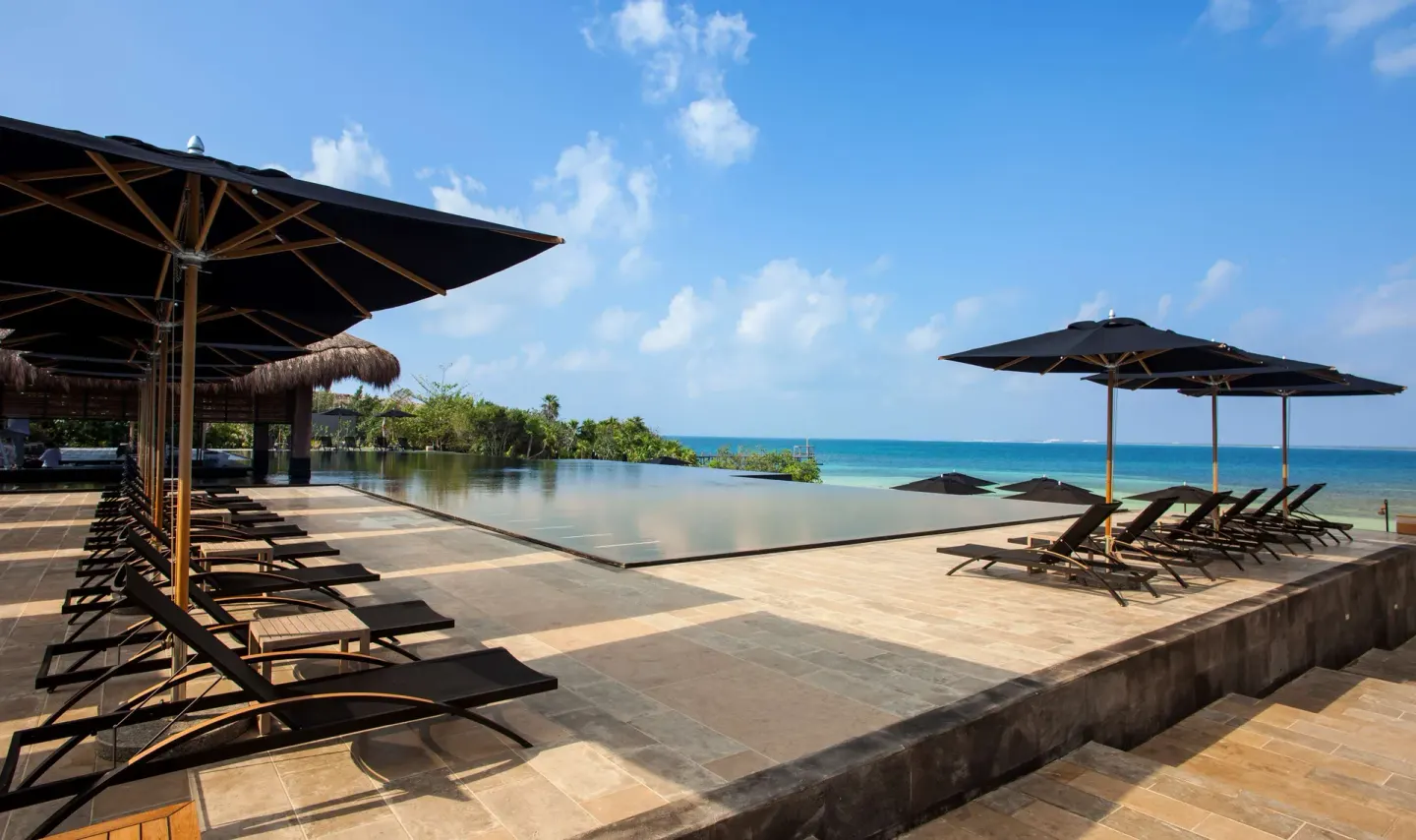 Pool loungers and umbrellas surround an infinity pool facing the sea at Nizuc Resort and Spa.