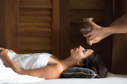 Spa treatment with warm oil poured onto a guest's forehead at Nizuc Resort and Spa.