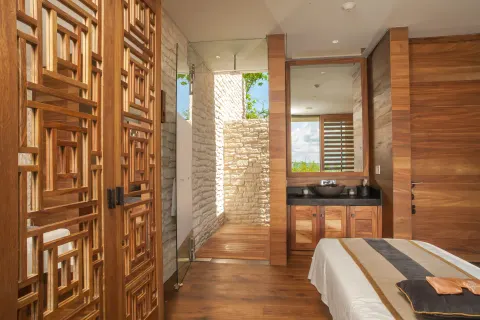 Spa treatment room with massage bed, vanity, wood screens, and stone shower at Nizuc Resort and Spa.