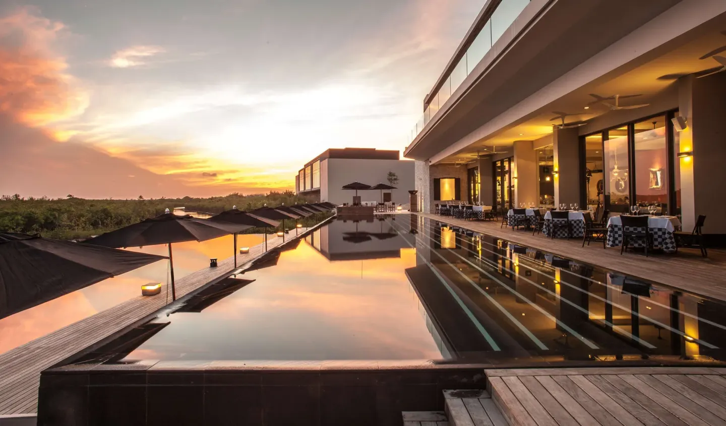 Sunset reflects in a long pool beside outdoor dining tables at Nizuc Resort and Spa.