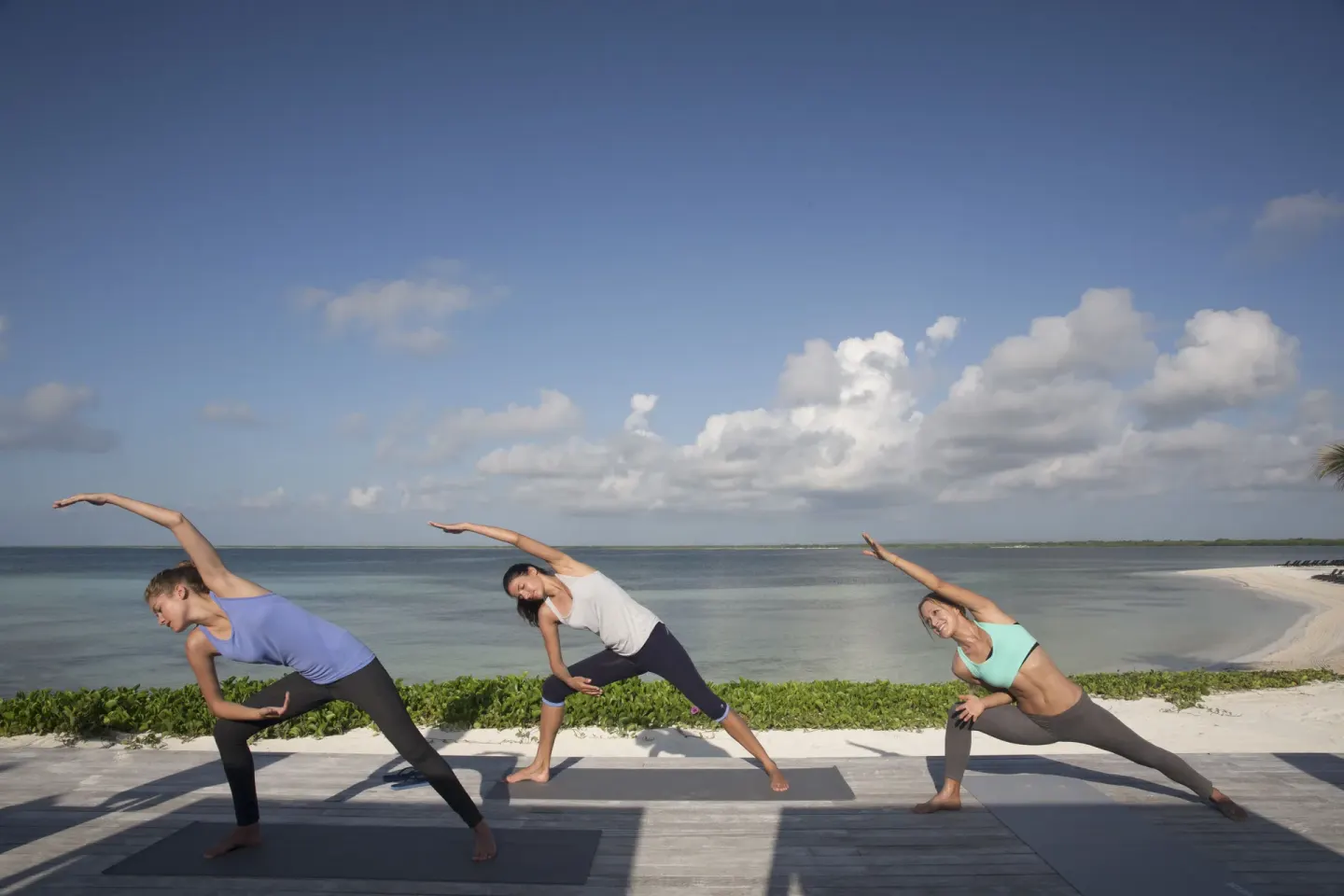 Three people practicing yoga on a deck overlooking the water at Nizuc Resort and Spa.