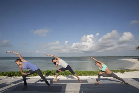 Three people practicing yoga on a deck overlooking the water at Nizuc Resort and Spa.