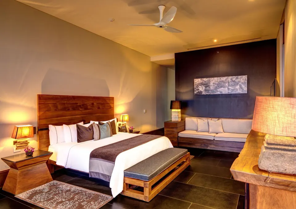 Penthouse king bedroom with warm lighting, sofa and ceiling fan at Nizuc Resort and Spa.