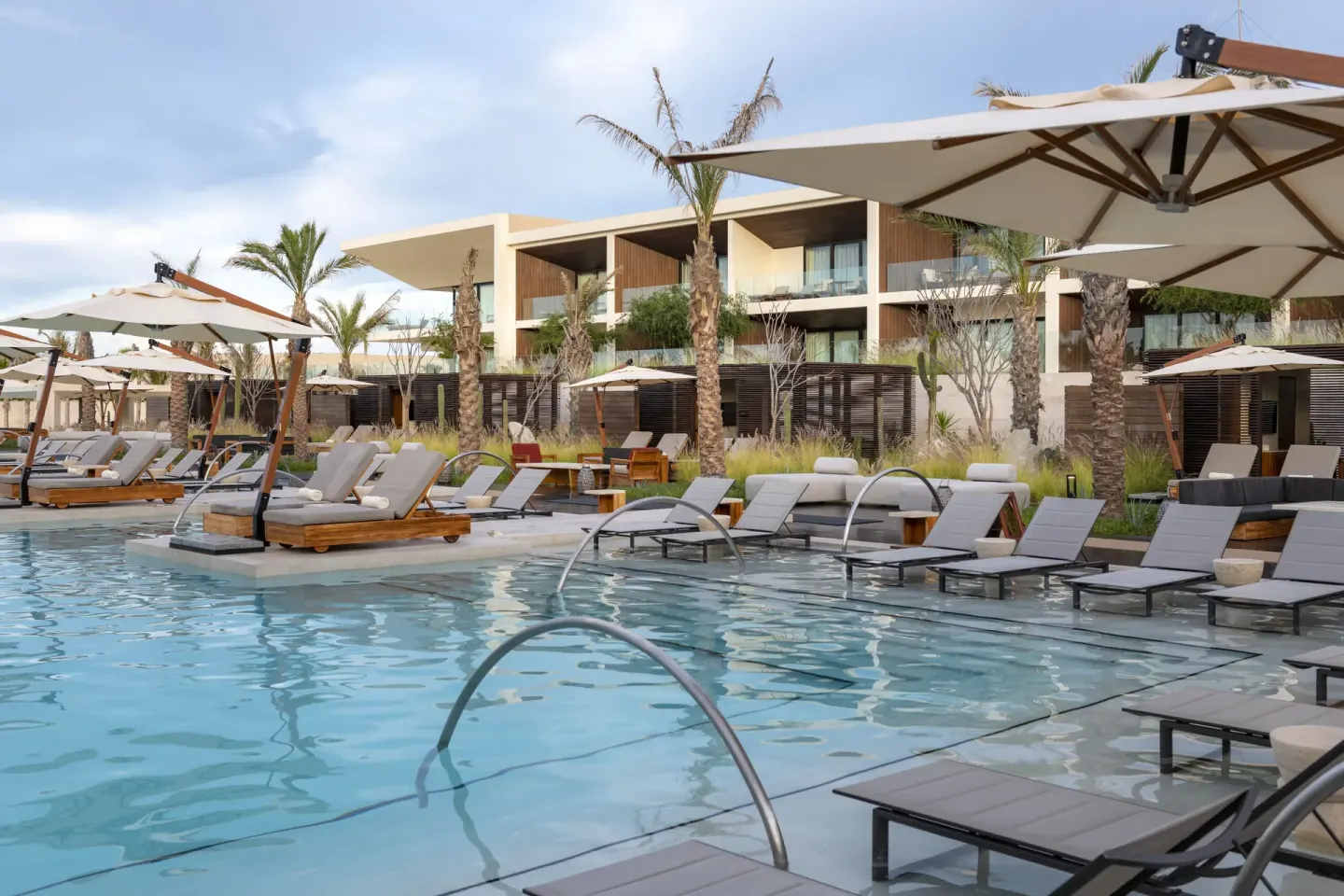 Poolside loungers, umbrellas and guest room balconies at Nobu Hotel Los Cabos.