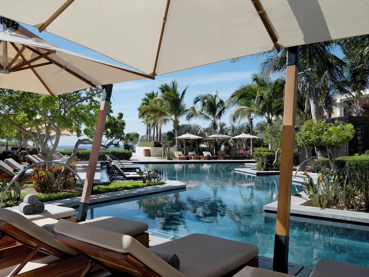 Shaded pool loungers with palm trees and cabanas at Nobu Hotel Los Cabos.