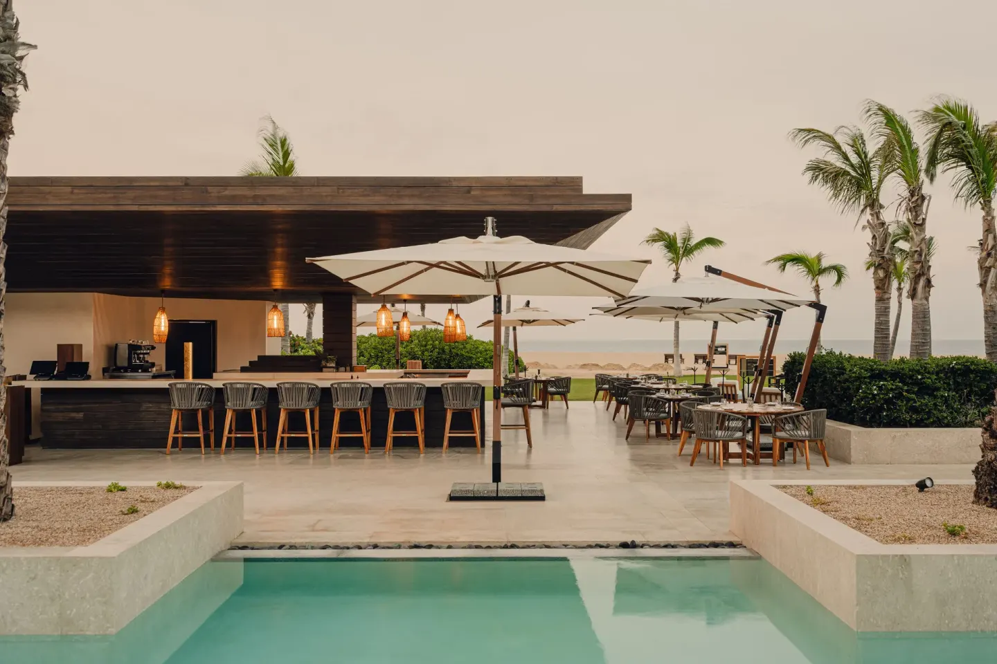 Poolside bar with umbrellas and ocean beyond at Nobu Hotel Los Cabos.