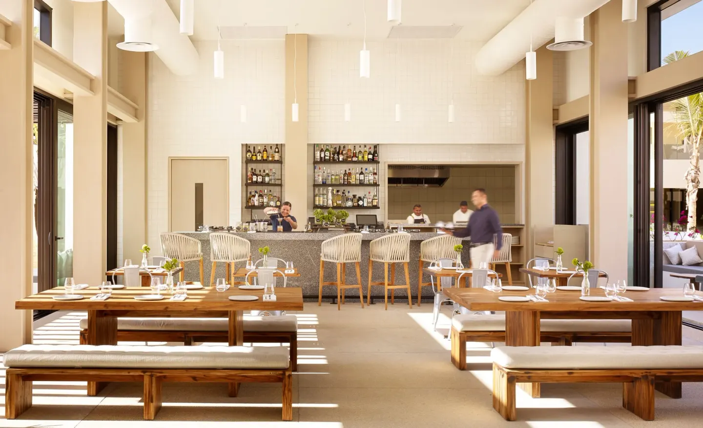 Sunlit restaurant dining room with bar and open kitchen at Nobu Hotel Los Cabos.
