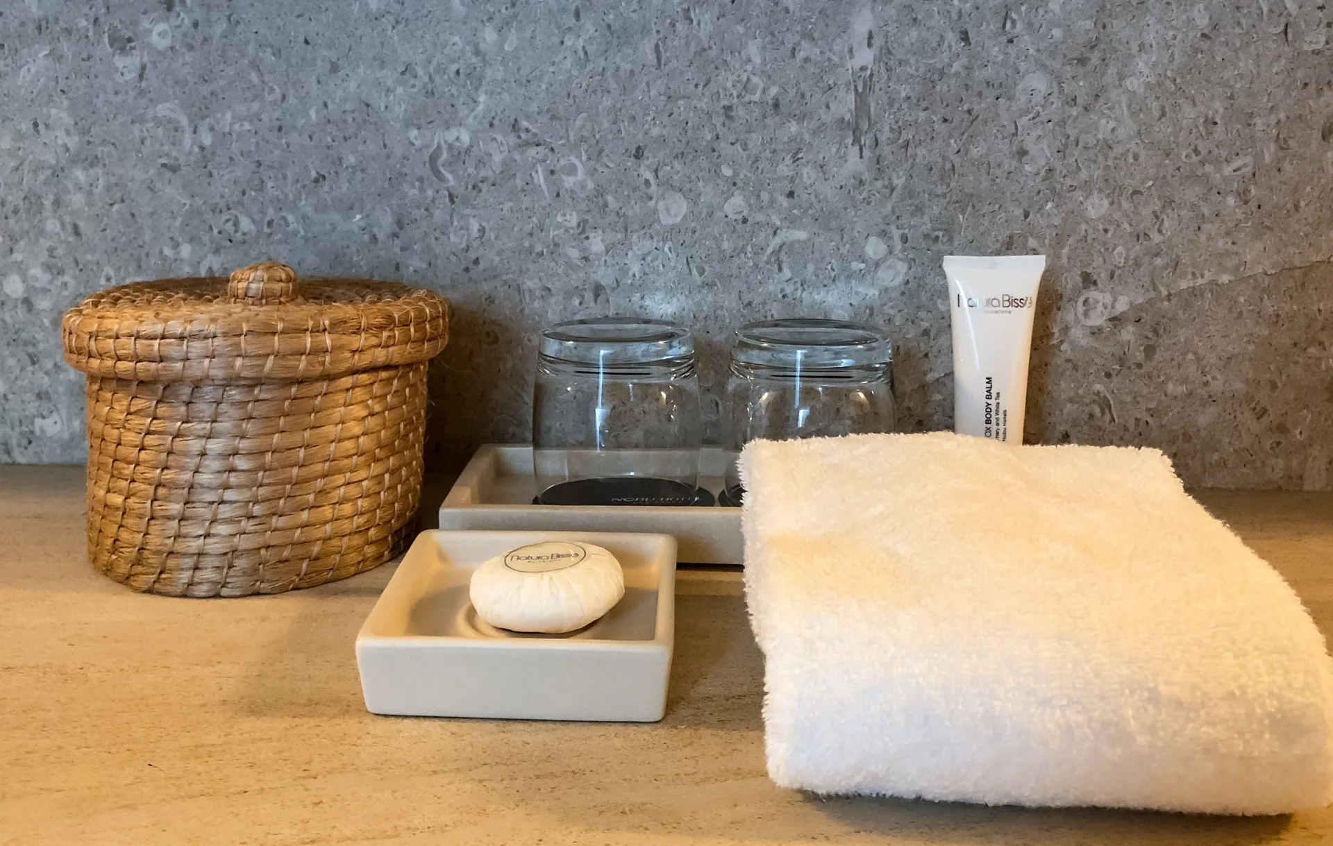 Deluxe Room bathroom counter with towel, glasses, soap, and basket at Nobu Hotel Los Cabos.
