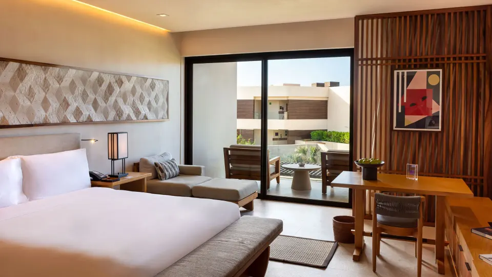 Deluxe Room king bed with balcony seating visible through glass doors at Nobu Hotel Los Cabos.