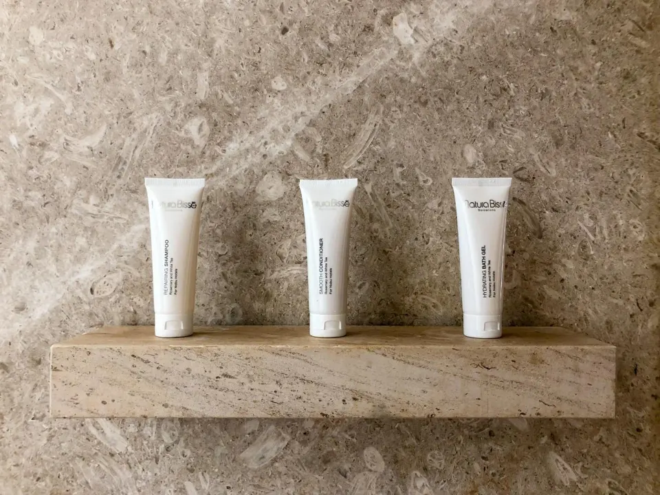 Three bath amenity tubes on a stone shelf in a deluxe room at Nobu Hotel Los Cabos.