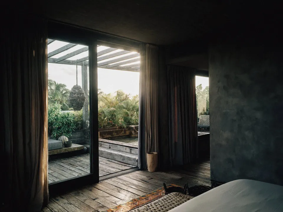 Sliding glass doors from a dark bedroom opening to a planted deck and plunge pool at Nômade Temple Tulum