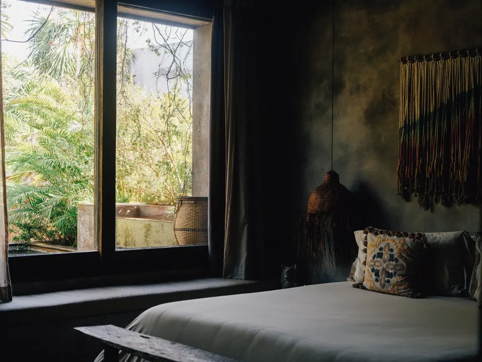Bedroom with bed and outdoor tub visible through the window at Nômade Temple Tulum