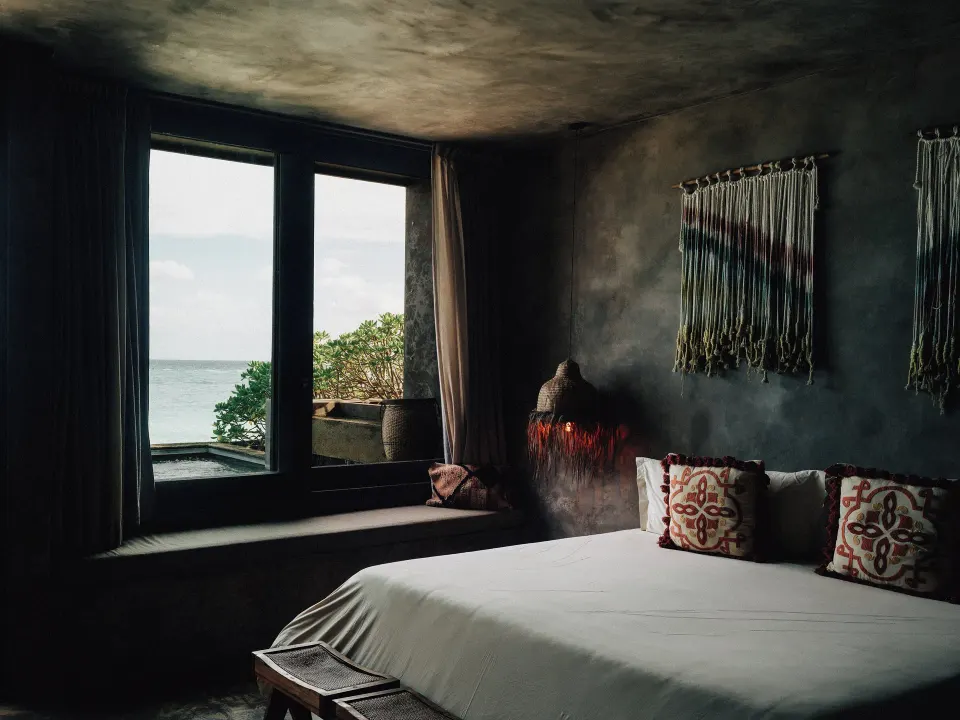 King bed beside a window with ocean glimpses in a guest room at Nômade Temple Tulum