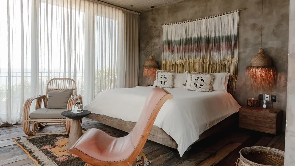 King bed with floor-to-ceiling curtains, armchairs and woven decor at Nômade Temple Tulum