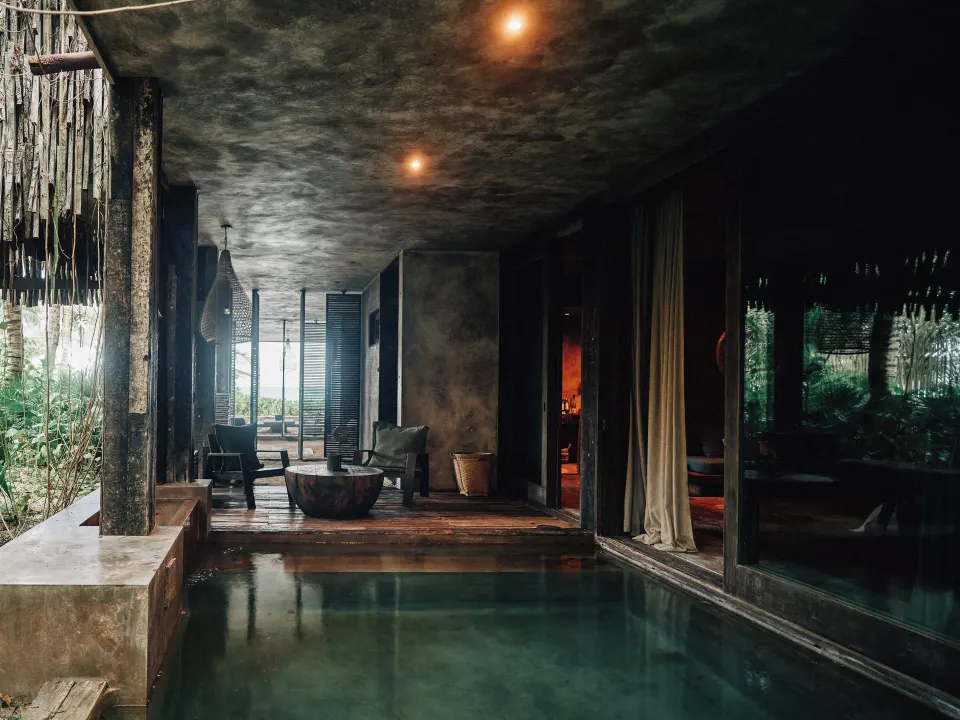 Covered living area beside a long plunge pool with seating at Nômade Temple Tulum