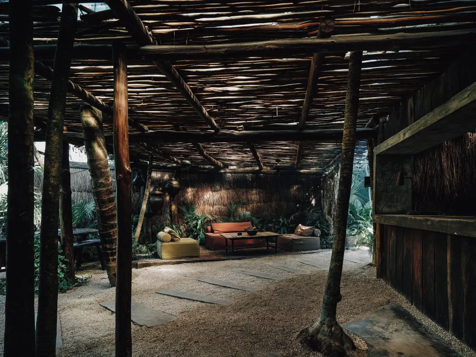 Covered seating area with low sofas and a reed ceiling at Nômade Temple Tulum