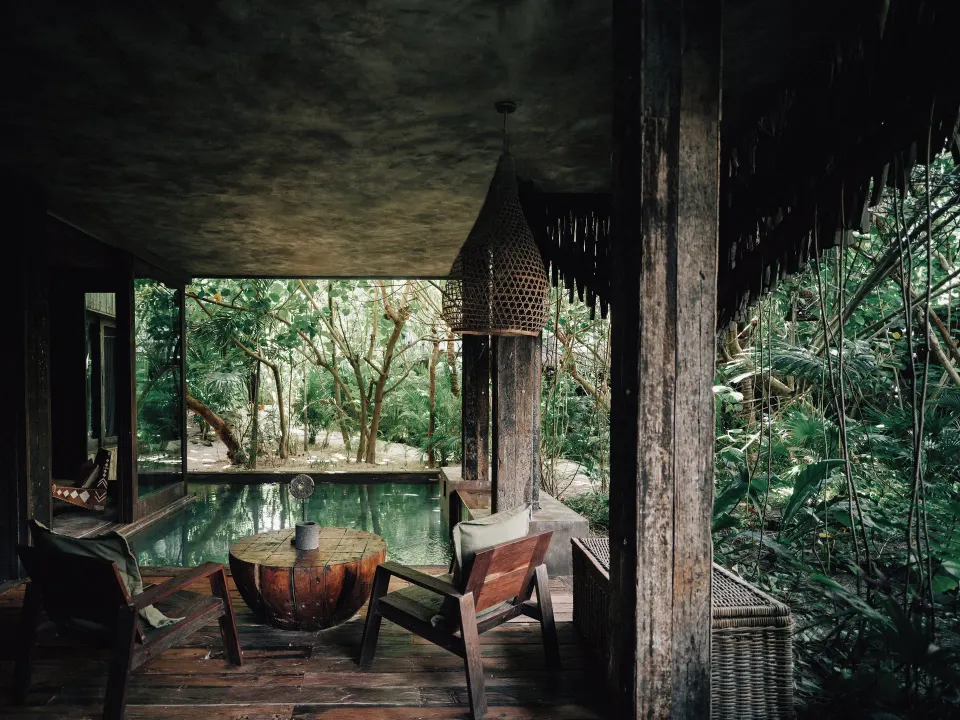 Covered terrace with wooden chairs overlooking a private pool and jungle at Nômade Temple Tulum