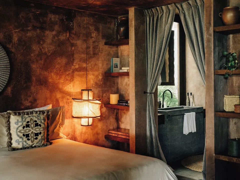 Cozy bedroom corner with soft lighting and a view into the bathroom at Nômade Temple Tulum