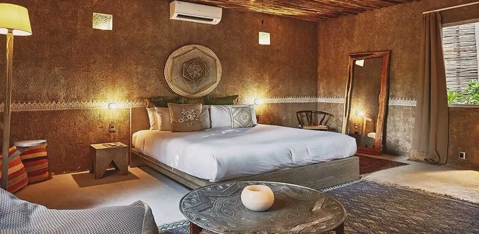 Large king bed and seating area with woven decor in a suite at Nômade Temple Tulum