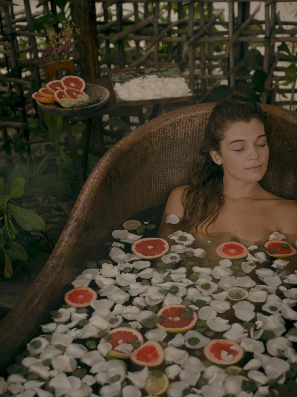 Woman reclining in a floral bath with fruit and petals at Nômade Temple Tulum
