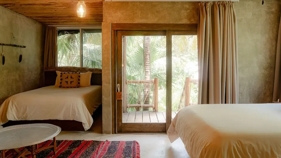 Bright guest room with two beds and a balcony visible through a sliding door at Nômade Temple Tulum