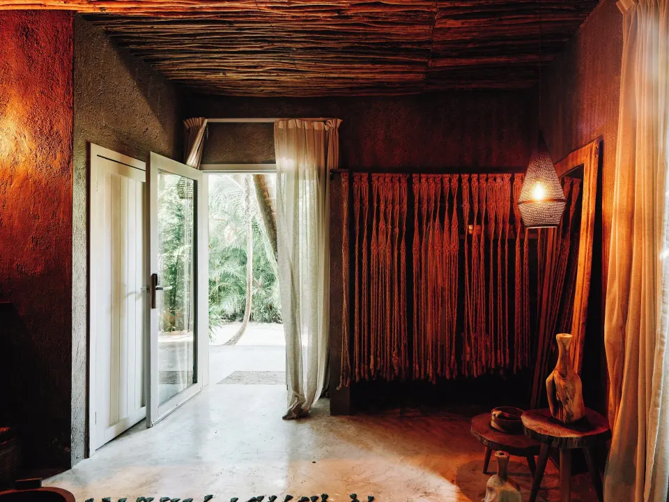 Entrance and interior of a rustic guest room at Nômade Temple Tulum with draped textiles