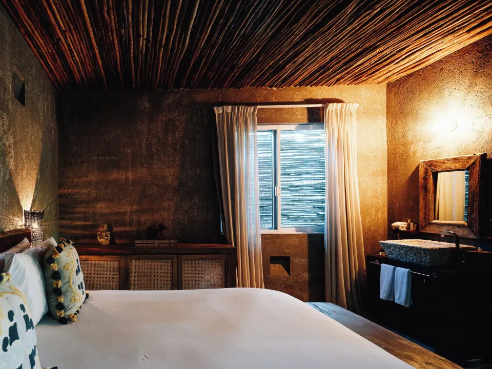 King bed and sink with woven ceiling in a warm-toned suite at Nômade Temple Tulum