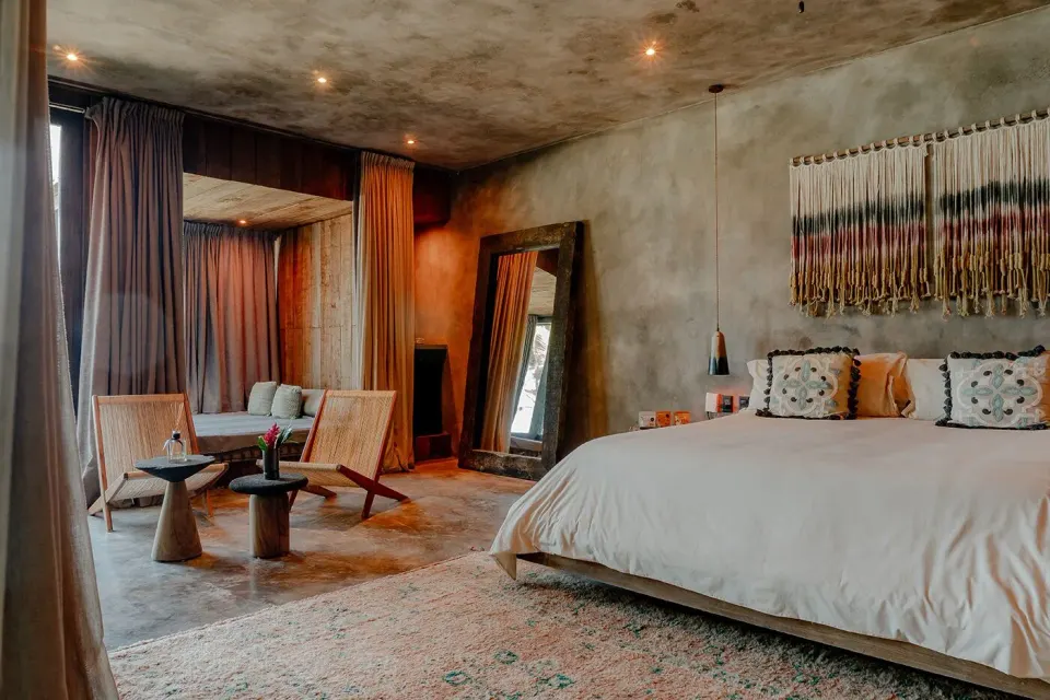 Corner view of a king bed and seating area in a guest room at Nômade Temple Tulum