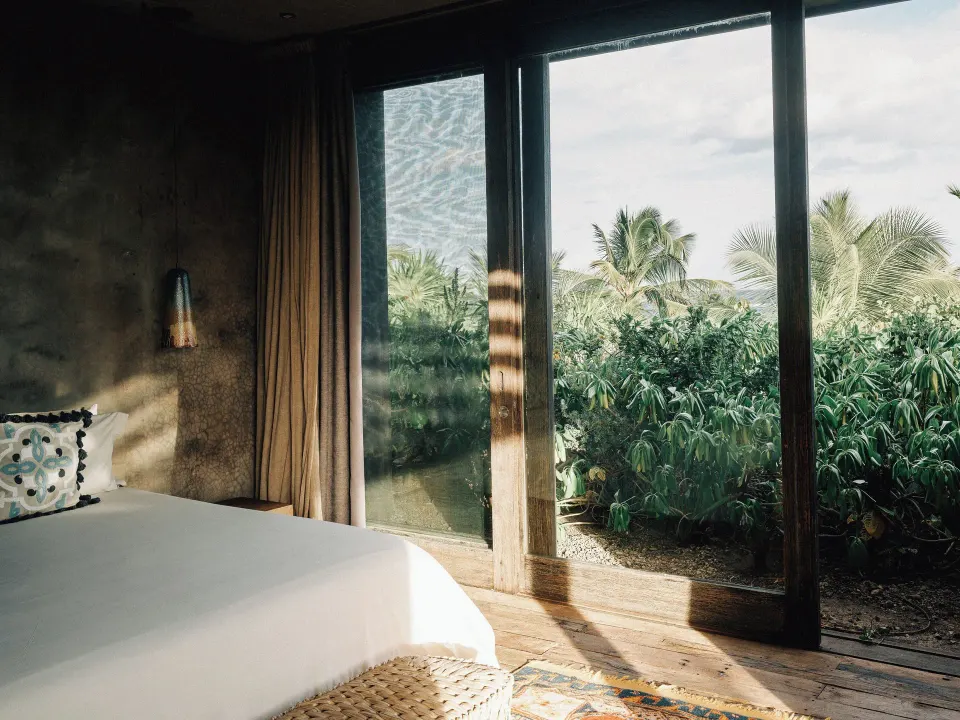 King bed beside floor-to-ceiling glass doors opening to tropical foliage at Nômade Temple Tulum