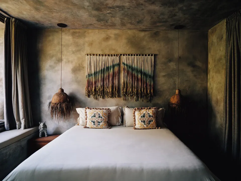 King bed with woven wall hanging and pendant lamps in a guest room at Nômade Temple Tulum