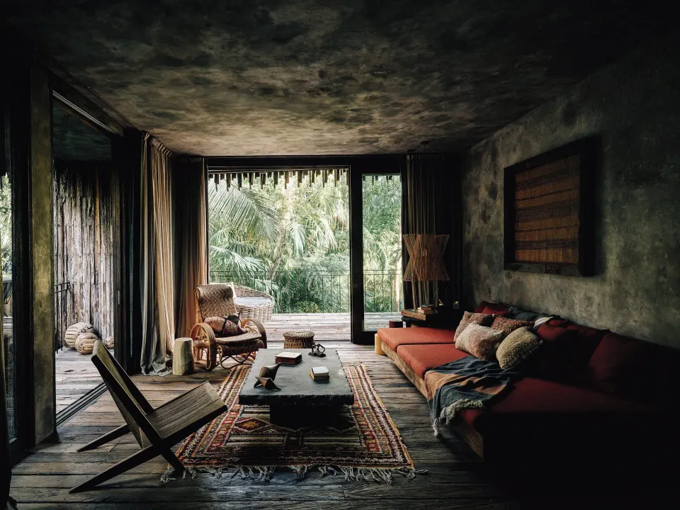 Living room with low sofa and deck opening onto palms at Nômade Temple Tulum