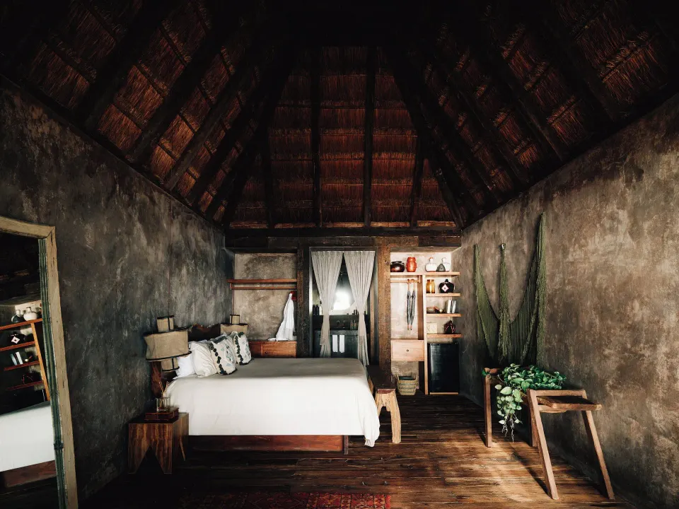 Spacious guest room with king bed, wooden floors and thatched roof at Nômade Temple Tulum