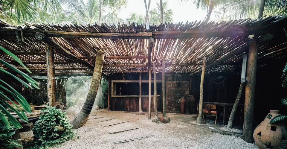 Thatched outdoor lounge area with wooden posts and gravel floor at Nômade Temple Tulum