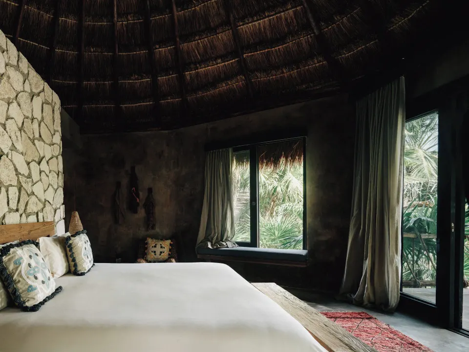 King bed beneath a thatched palapa ceiling in a guest room at Nômade Temple Tulum