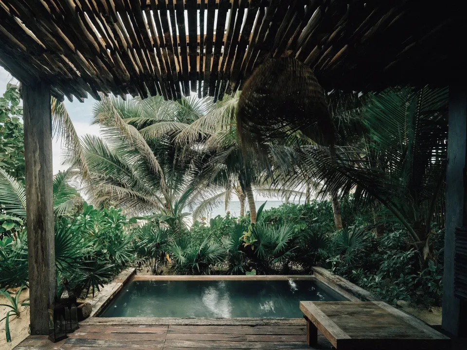 Plunge pool framed by a rustic pergola with palms and ocean beyond at Nômade Temple Tulum