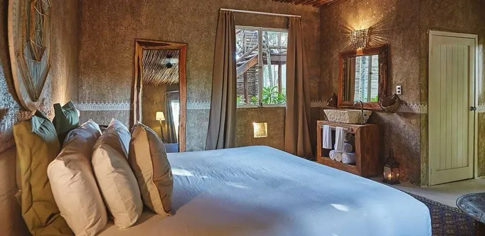 Cozy king bed with textured walls and wooden accents at Nômade Temple Tulum