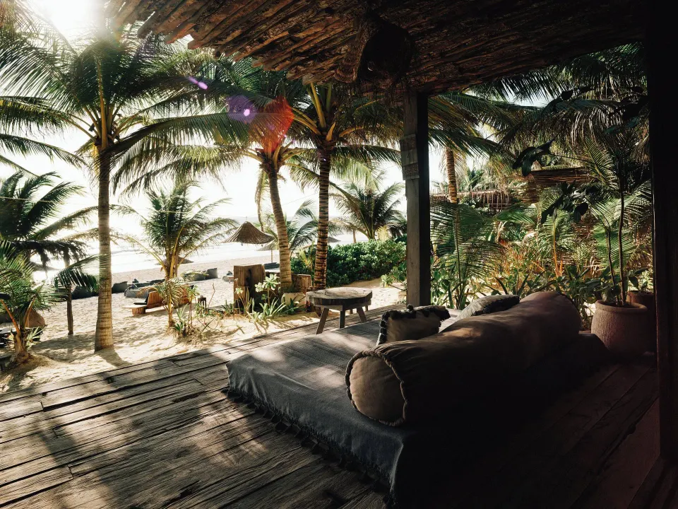 Shaded beachfront deck with daybed and palm trees at Nômade Temple Tulum